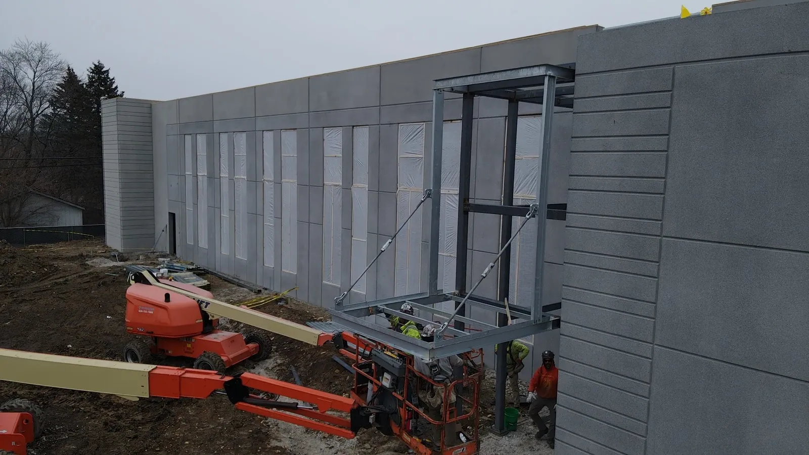 North Aurora Fire District Headquarters: ironworkers on boom lifts setting a steel frame against the precast facade